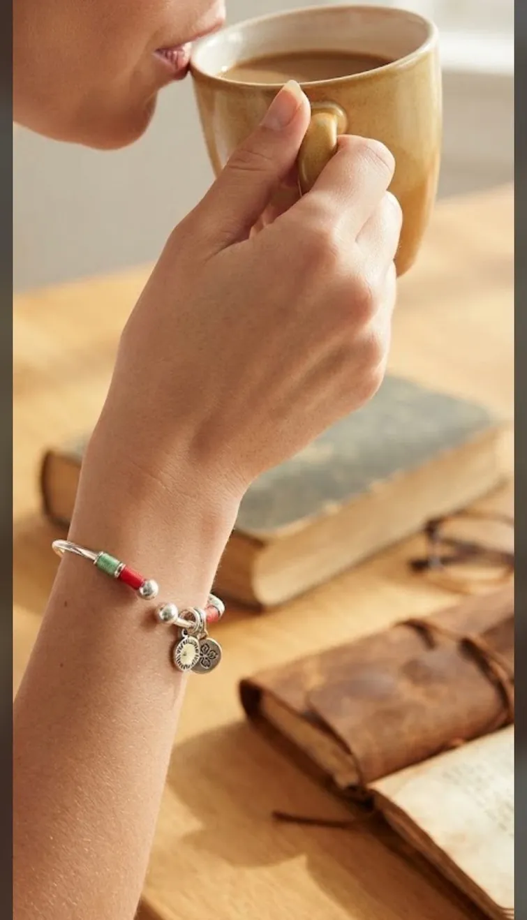 A silver-tone bangle on the wrist of a hand lifting a cup of coffee