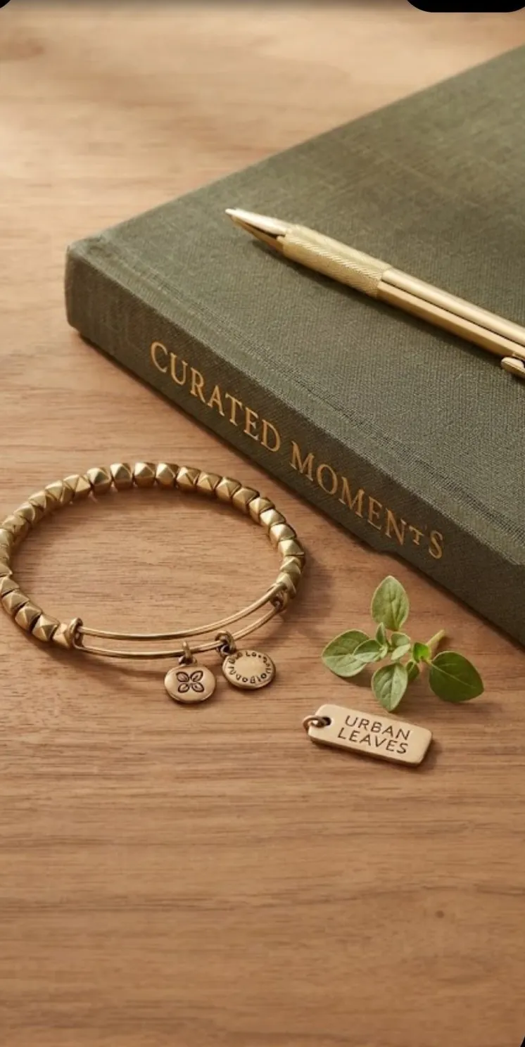 A gold-tone beaded bangle on a table with a bound book, a pen and the Urban Leaves tag