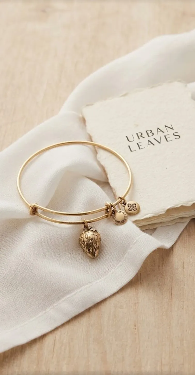 A gold-tone bangle on white linen with the Urban Leaves card